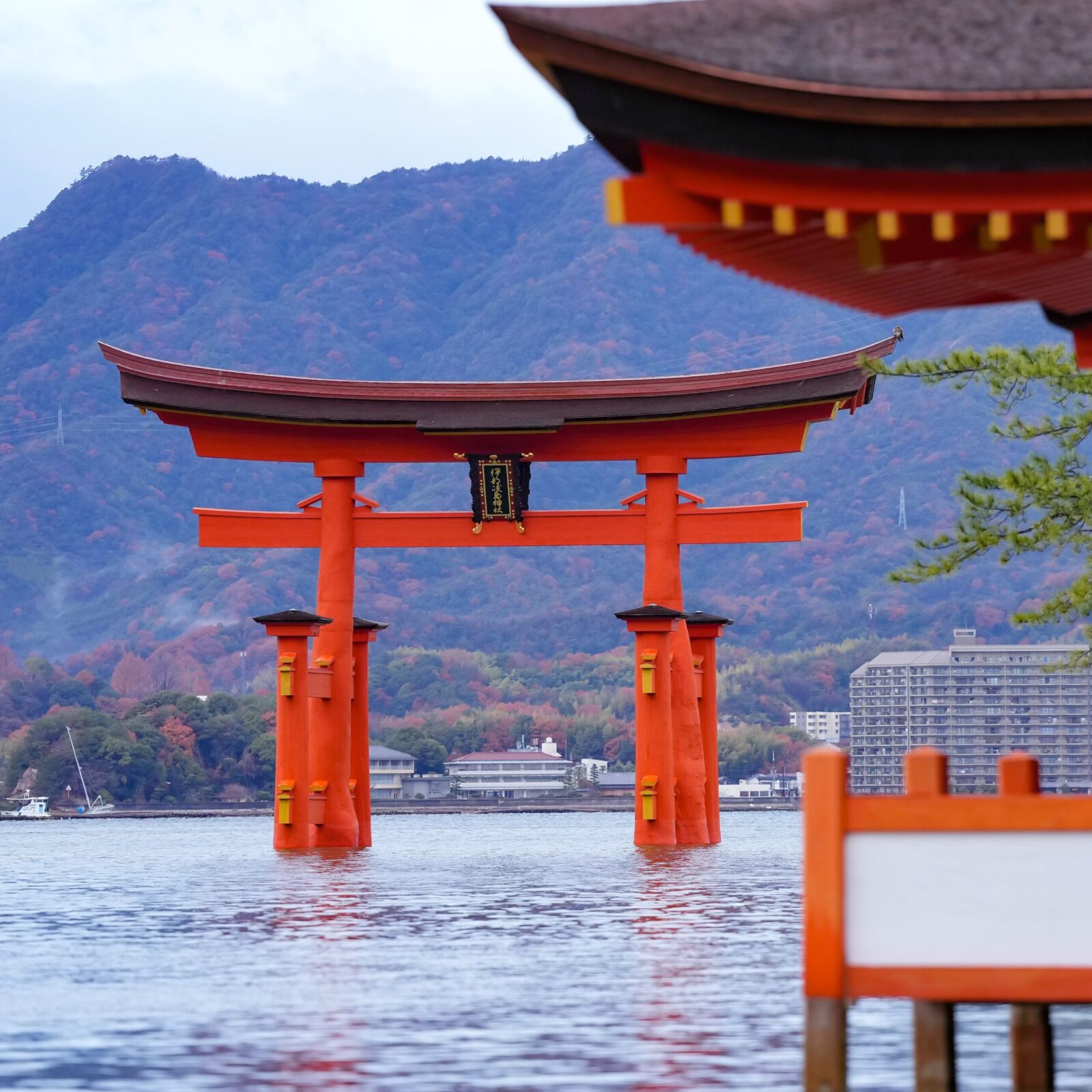 L'iconico cancello torii "galleggiante" del santuario di itsukushima, con uno sfondo di montagne lussureggianti e cieli nuvolosi.